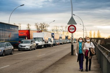 Almanya ile Fransa arasındaki sınırda koruyucu maske takan iki kadının yürüdüğüne odaklı olmayan bakış açısı.