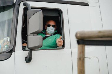 Mercedes-Benz Actros 'ta koruyucu maske takan kamyon şoförü OK işareti gösteriyor.