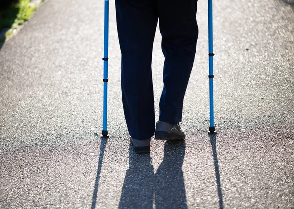 Rear view of senior male walking using walking sticks on the street — Stock Photo, Image