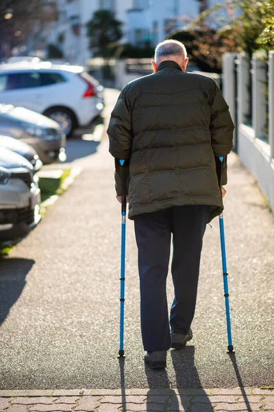 Vista trasera de un hombre mayor caminando usando bastones en la calle — Foto de Stock
