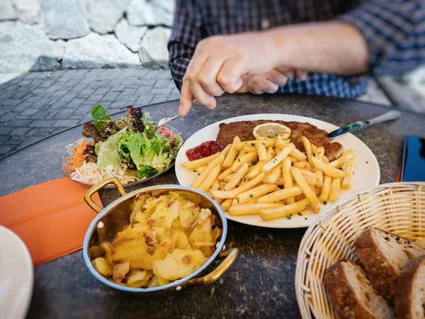 Man hand äta från stora maträtt tyska schnitzel med bakade pommes frites — Stockfoto