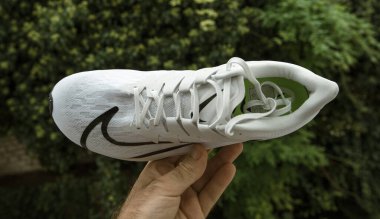 Pov erkeği, Nike modeli Zoom Rival Fly tarafından üretilen, siyah logolu kadınlar için üretilen yeşil arka plan profesyonel koşu ayakkabısına karşı el ele tutuşuyor.