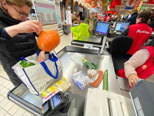 Mujer en el embalaje en su bolsa de múltiples productos comprados en el supermercado Auchan francés — Foto de Stock