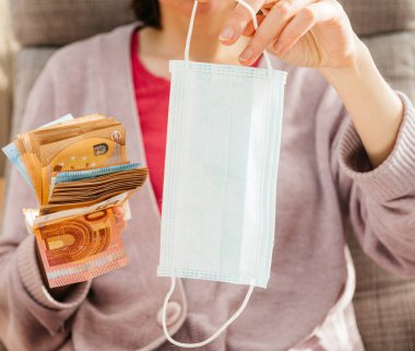 Bir yığın para teklif eden kadın. Banknotlar. Ameliyat prosedürü. Tıbbi yüz maskesi.