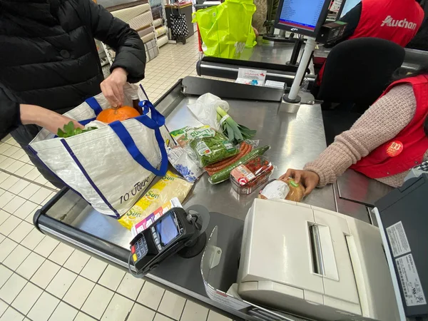 Mujer en el embalaje en su bolsa de múltiples productos comprados en el supermercado Auchan francés — Foto de Stock