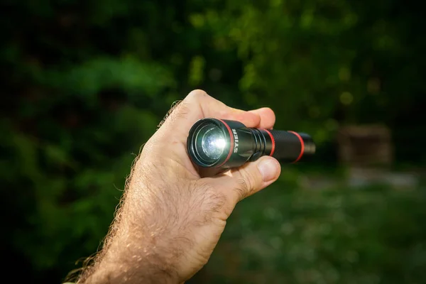 Ανδρικό χέρι κρατώντας νέο μίνι LED Stier φακό φακό πράσινο φόντο δάσος — Φωτογραφία Αρχείου