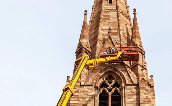 Telephoto view of team workers on tall lifting platform church repair — Stock Photo, Image