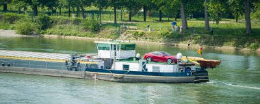 Ren nehrinde kırmızı elektrikli Tesla arabasıyla kum kömürü taşıyan bir tanker.