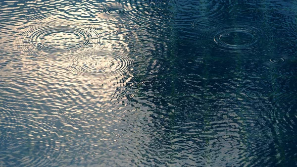 Rain drops on blue water swimming pool