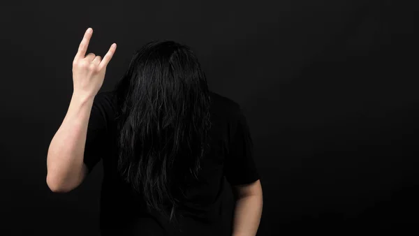 Rocker man długie włosy i co znak strony rock and roll i potrząsanie głową z czarnym kolorze t-shirt i ciemnym tle papieru w studio, które reprezentują styl muzyki, takich jak punk lub heavy metal — Zdjęcie stockowe