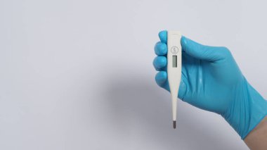 Doktorun ellerinde dijital termometre beyaz renk. Tıbbi eldiven giyiyor. Açık mavi renk. Selsiyus veya fahrenhayt derecesi salgın için kontrol edilebilir.