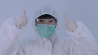 PPE kostümlü Asyalı kadın doktor ve kameranın önünde parmaklarını tıbbî gözlüklü, maskeli, eldivenli parmaklarıyla çok mutlu ya da tebrik edici ya da Corona virüsünü ya da covid-19 problemini çözme başarısını temsil ediyor..