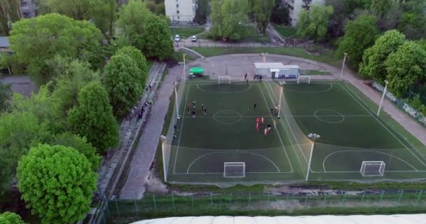 Vista aérea del campo de fútbol por la noche con jugadores de fútbol amateur jugando el juego en la ciudad. — Vídeo de stock