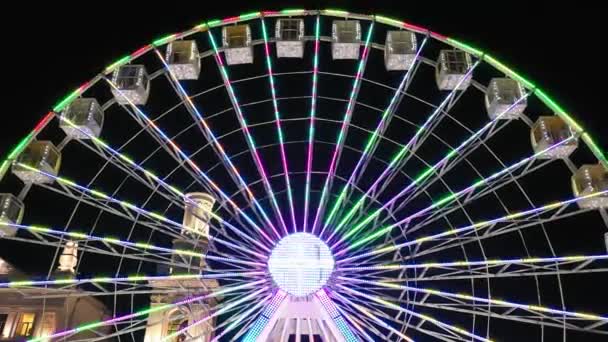 Paseo en noria brillantemente iluminado girando por la noche en un carnaval, parque de atracciones, parque temático, feria, parque de emociones. — Vídeo de stock