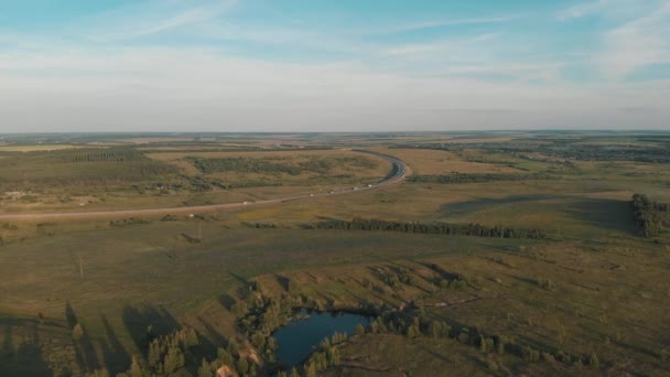 Drón repül át a kis tó körül ritka növényzet kék ég és fehér felhők. Átível az autópályán. — Stock videók