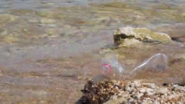 Uma garrafa de plástico na praia. Garrafa de plástico de lixo deixada na praia. Concentre-se em garrafa de plástico, ondas do mar no fundo, mar e poluição costeira — Vídeo de Stock