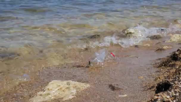 Botella de plástico en la playa. Botella de plástico basura izquierda en la playa. Enfoque en la botella de plástico, las olas marinas en el fondo, el mar y la contaminación costera — Vídeos de Stock