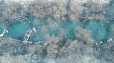 Güzel bir manzaranın üzerinde uçuyor. Kışın dere ve park karla kaplıydı. Drone çözülmemiş turkuaz nehrin üzerinde uçuyor. Ormandaki Kış Gölü. Kar yağıyor