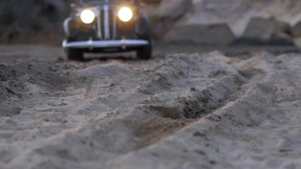 Den retro bil kører under ekstreme forhold på en sandet vej med forlygter på, hvor du kan observere affjedringen, og hvordan dækkene opfatter svært. Retro stil video – Stock-video
