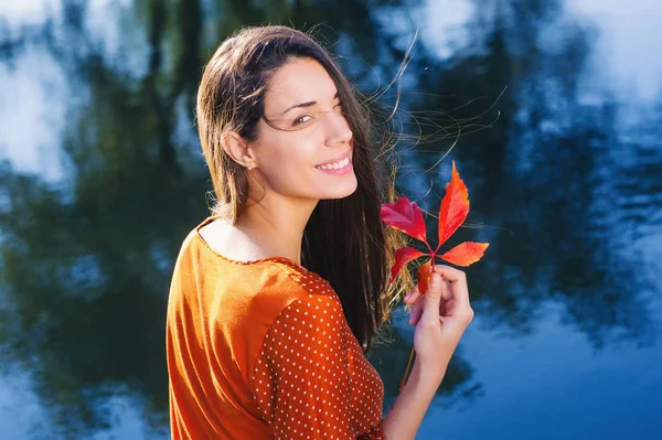 Beautiful smiling young woman with autumn red leaf — Stock Photo, Image