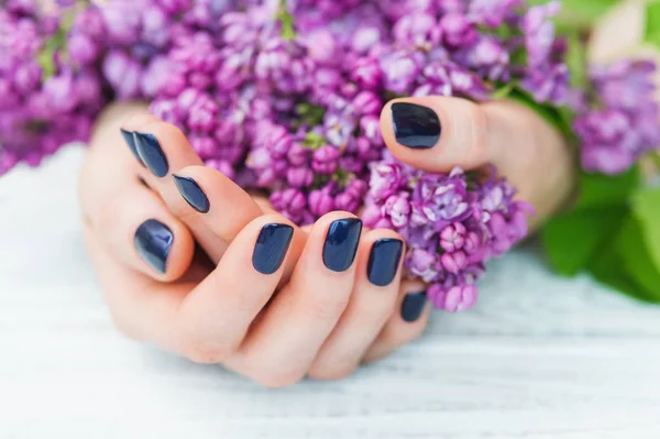 Vrouw handen met donker blauwe manicure en lila bloemen — Stockfoto