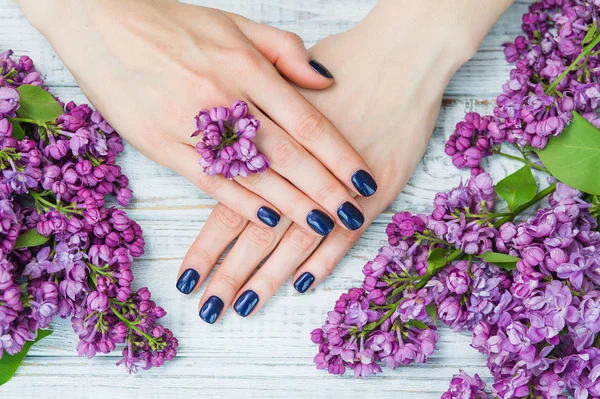 Kvinna händer med mörk blå manikyr och lila blommor — Stockfoto