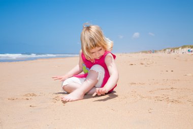küçük çocuk oturma ve kum plajı üzerinde parmak ile yazma