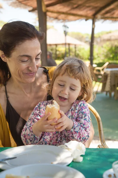 Kleines Kind isst Brot sitzend auf Frauenbeinen — Stockfoto