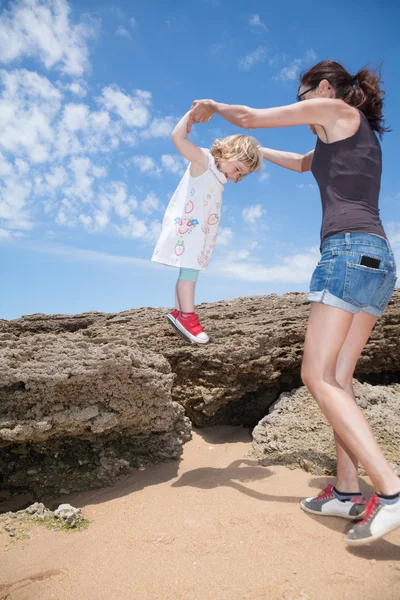 Klein kind houden handen vrouw springen van rotsen — Stockfoto