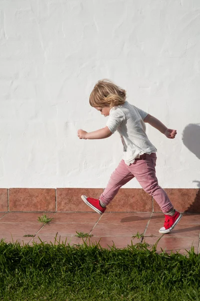 Ходячий маленький ребенок в саду над белой стеной — стоковое фото