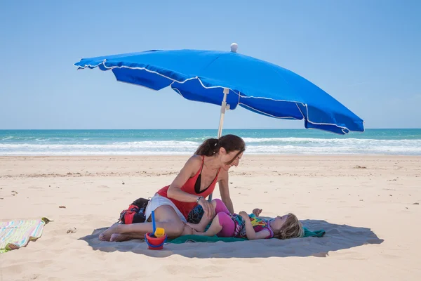 妈妈和小女孩倒在海滩的蓝色阳伞 — 图库照片