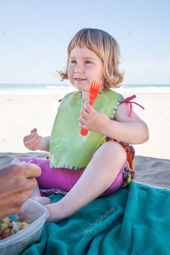 little child eating with fork in hand at beach