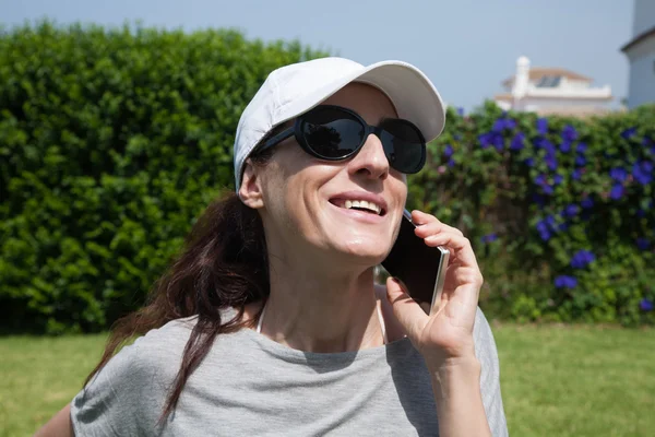 Mujer gorra blanca sonriendo escuchando el teléfono en el jardín — Foto de Stock