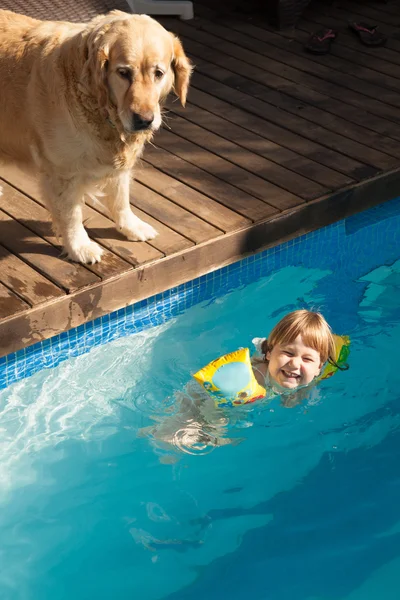 Смеющийся ребенок в бассейне с водой и собака — стоковое фото