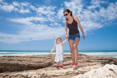 Anne ve çocuk tutuşup okyanus yanındaki yürüyüş