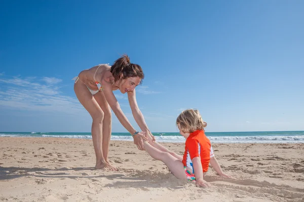 Mujer divertida arrastrando niño en la playa de arena —  Fotos de Stock