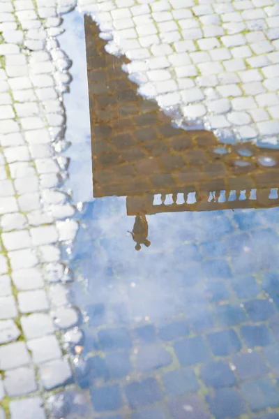 Estatua romana reflejada en agua de charco sobre adoquín —  Fotos de Stock