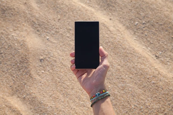 Telefone na mão sobre areia — Fotografia de Stock