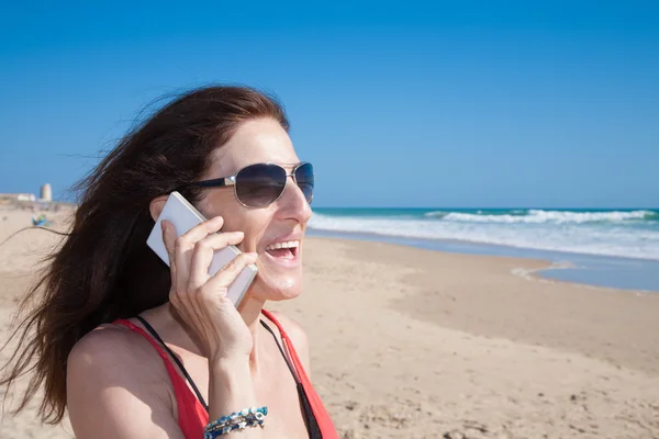 Woman with sunglasses talking on mobile at beach — Stock Photo, Image