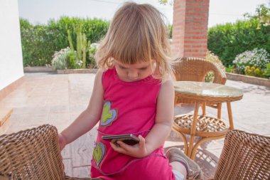 küçük kız cep telefonu izlemek hasır sandalye üzerinde diz çökmüş