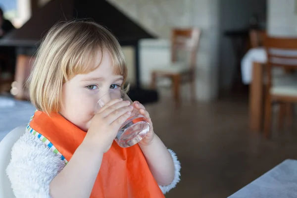 Pieni lapsi juomaveden lasi ravintolassa — kuvapankkivalokuva