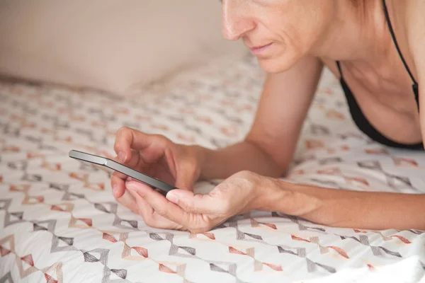 Smartphone in woman hands lying on the bed — Stock Photo, Image