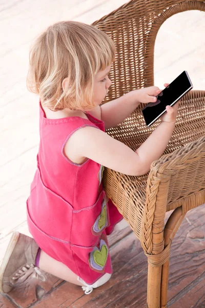 küçük kız cep telefonuyla hasır sandalye üzerinde diz çökmüş