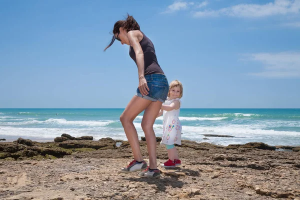 Mãe e criança caminhando sobre rochas ao lado do oceano — Fotografia de Stock