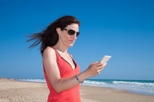 红衬衫的女人在海滩上使用移动电话 — 图库照片