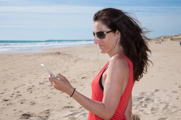 Czerwona koszula kobieta przy użyciu smartfona na plaży — Zdjęcie stockowe
