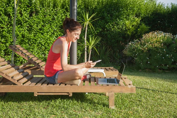 Kobieta z telefonem a komputerem na salonie drewniany leżak — Zdjęcie stockowe