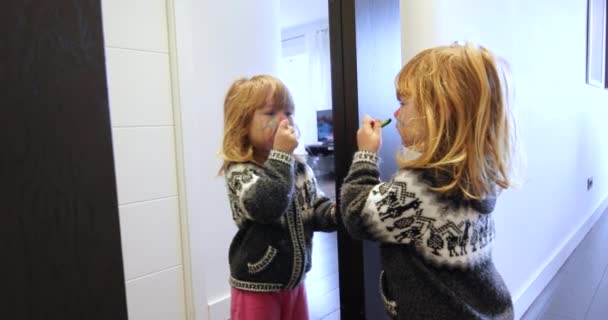 Счастливый ребенок рисует свое лицо, глядя в зеркало — стоковое видео