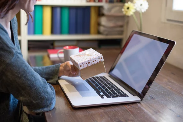 Женщина с подарком в руках смотрит ноутбук — стоковое фото