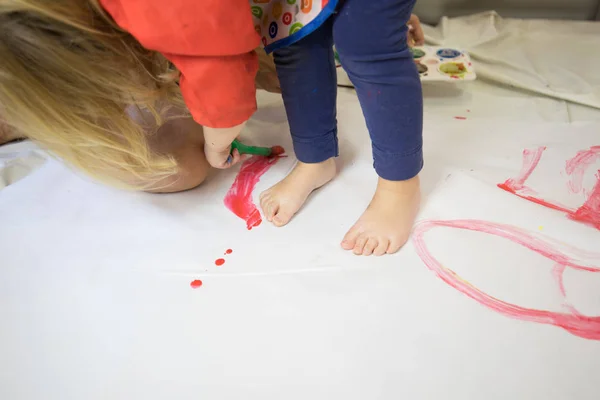 Barefoot child painting white paper with red watercolor — Stock Photo, Image